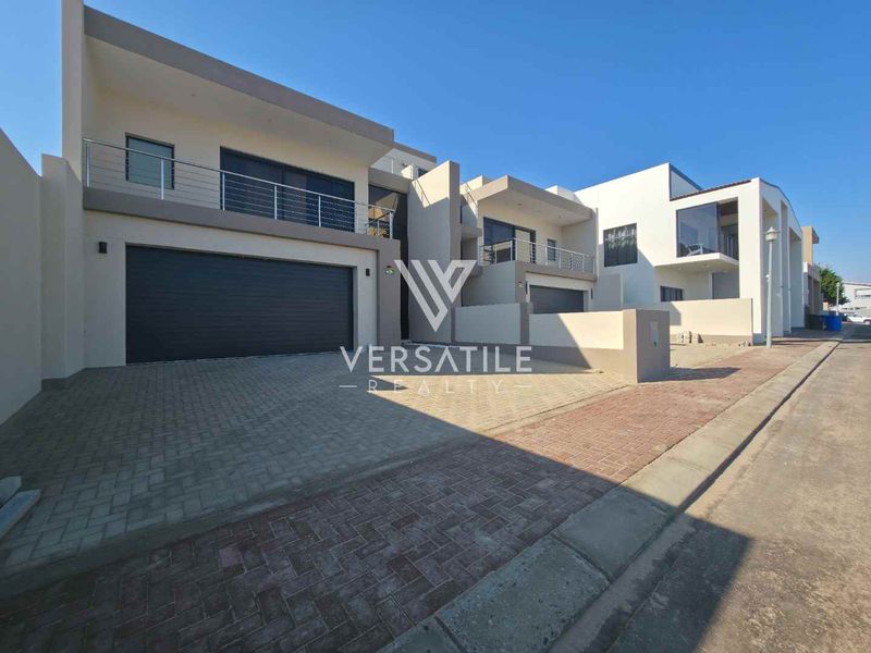 Modern double-story residential property featuring a paved driveway, double garage, and upper-level balconies with stainless steel balustrades.