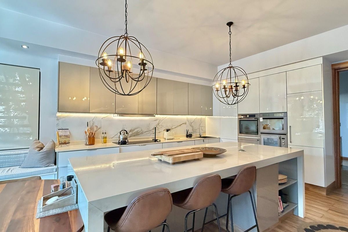 Modern open-plan kitchen featuring high-gloss cabinetry, stone countertops, a large central island, integrated appliances, and stylish spherical pendant lighting.