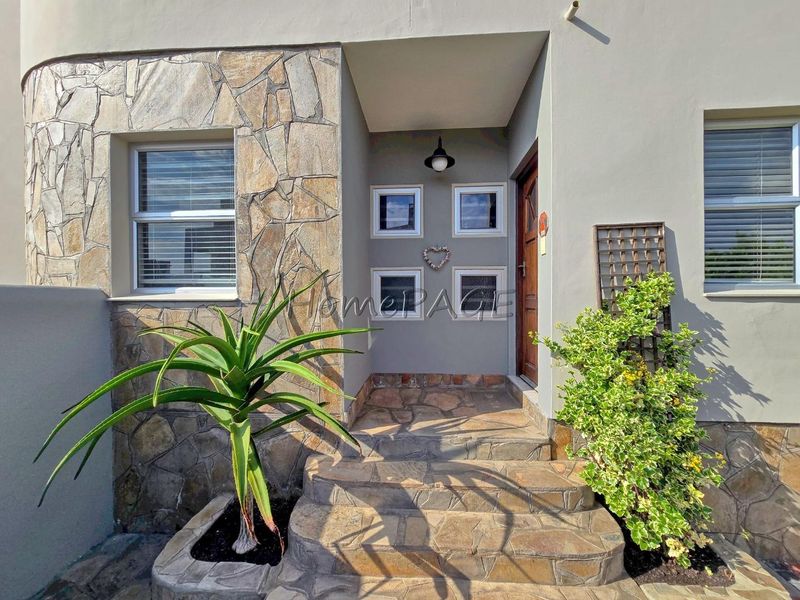 Front entrance featuring stone cladding, a timber door, and stone-paved steps with decorative glass block windows.