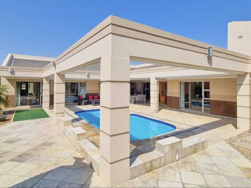 A well-maintained outdoor entertainment area featuring a swimming pool, covered patio with stone paving, and direct access to the home via sliding glass doors.