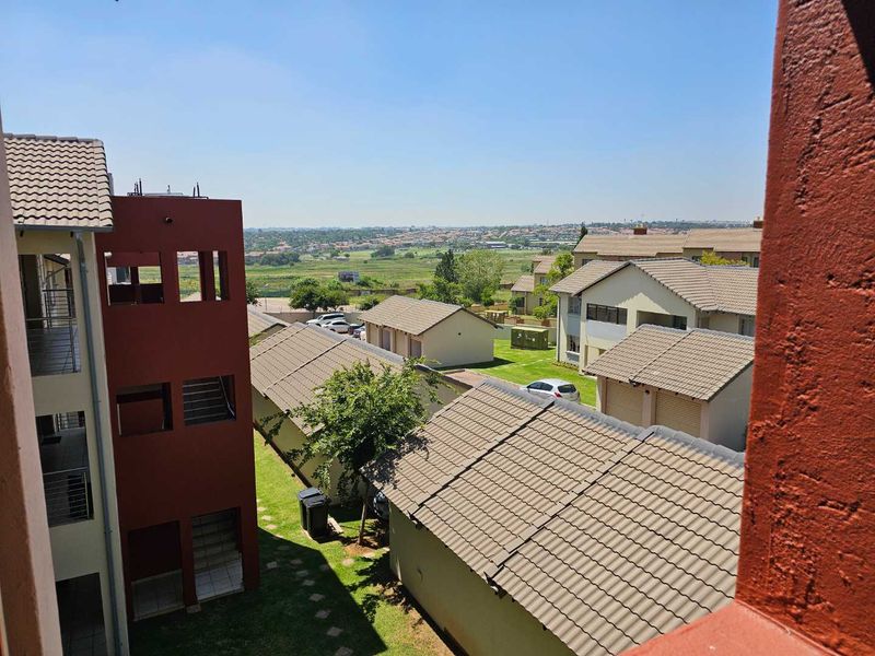 Elevated view overlooking the apartment complex grounds, featuring tiled roof structures and landscaped communal garden areas under a clear sky.