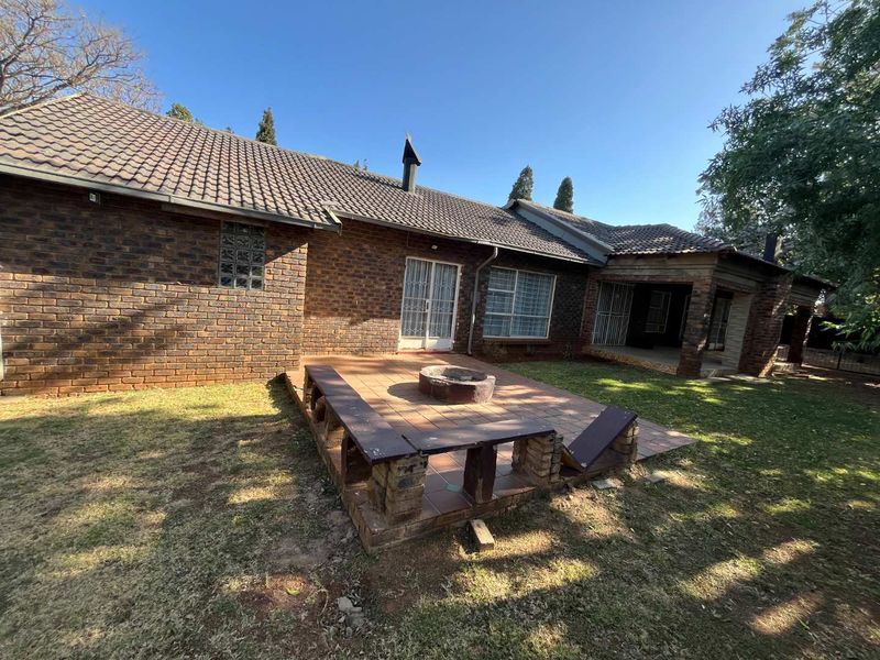 Rear exterior view featuring a brick facade, tiled roof, and a paved patio area with a built-in fire pit and brick seating.