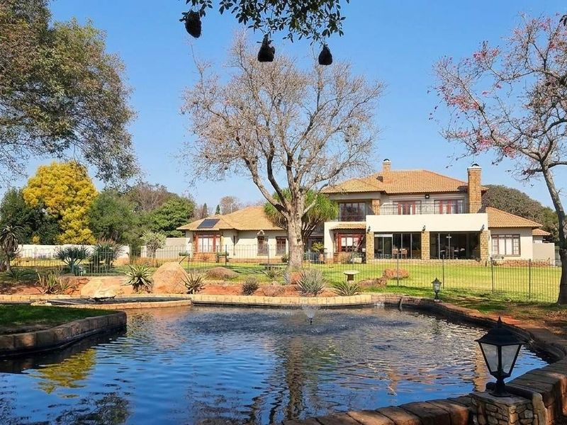 Spacious rear garden featuring a large pond with a fountain, manicured lawn, and a multi-story residence with a covered patio and tiled roof.