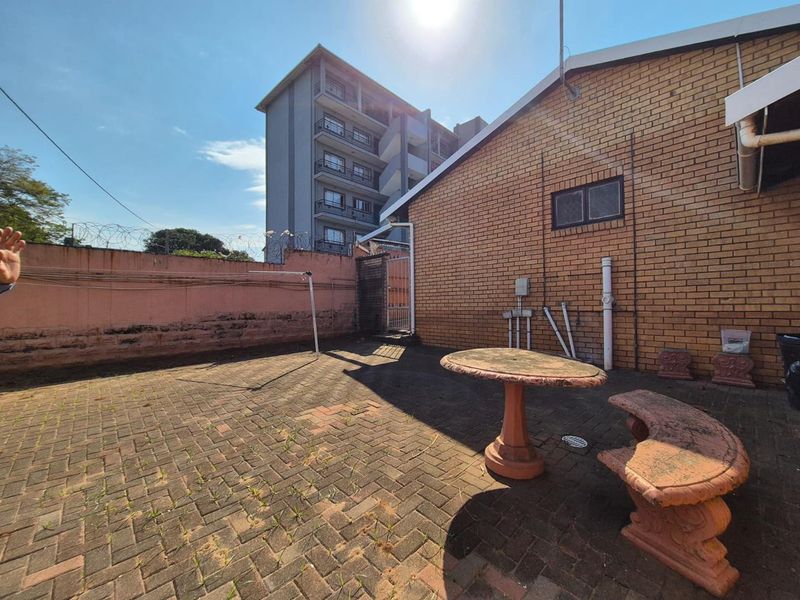 A paved rear courtyard area featuring a brick facade, perimeter wall with security fencing, and basic drainage infrastructure.