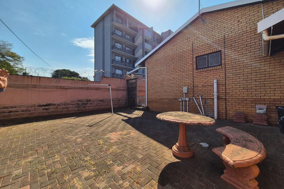 A paved rear courtyard area featuring a brick facade, perimeter wall with security fencing, and basic drainage infrastructure.