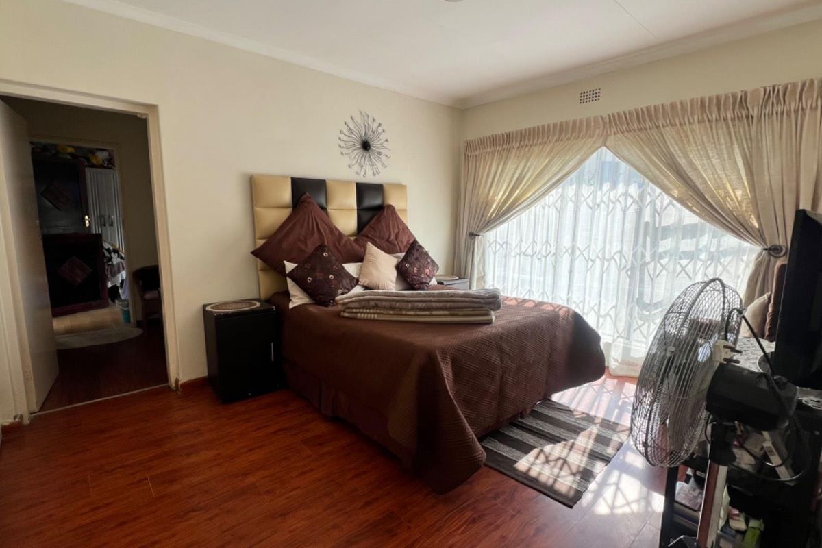 A bedroom featuring laminate wood flooring, a large window with security gate, and neutral wall finishes.