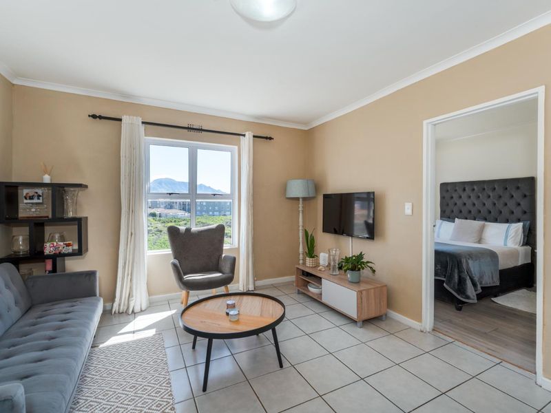 A well-lit living room featuring tiled flooring and a window with views, providing direct access to the adjacent bedroom.