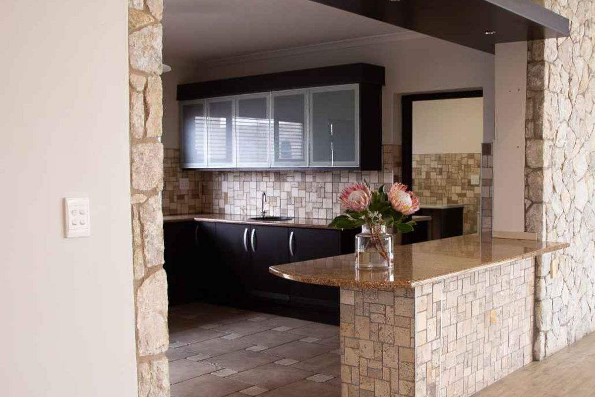 A well-defined kitchen featuring stone-clad accents, a granite breakfast bar, dark cabinetry, and a tiled backsplash, creating a distinct and functional culinary space.