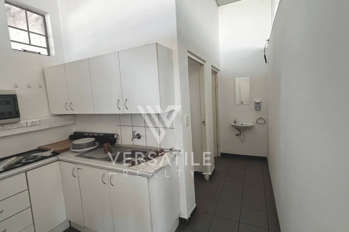 A functional kitchenette area featuring white cabinetry, a stainless steel sink, and tiled flooring, adjacent to a small washroom area.