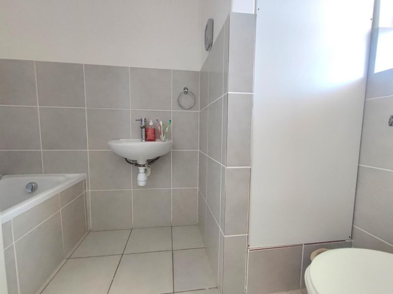 A functional bathroom featuring a wall-mounted basin, chrome mixer tap, and built-in bathtub with neutral ceramic tiling throughout.