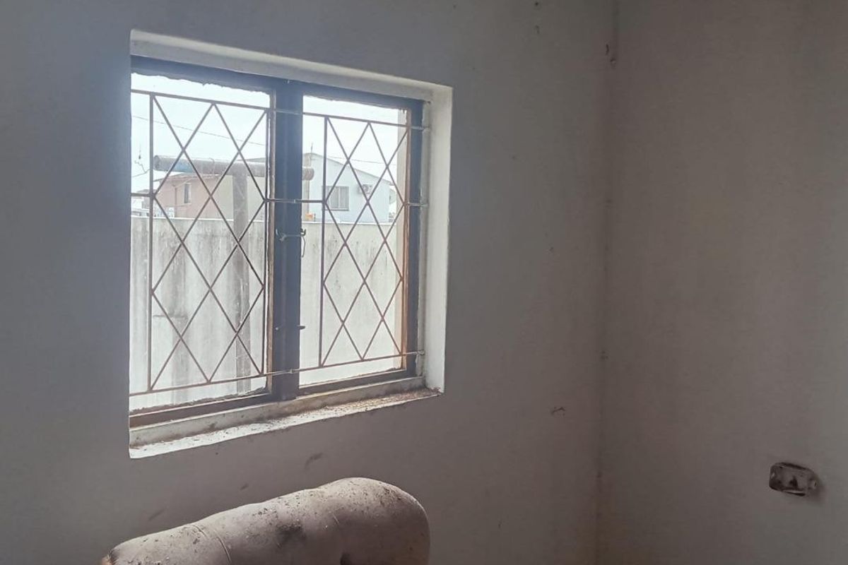 A vacant bedroom featuring a window with security bars, requiring cosmetic updates and wall repairs to improve its overall condition.