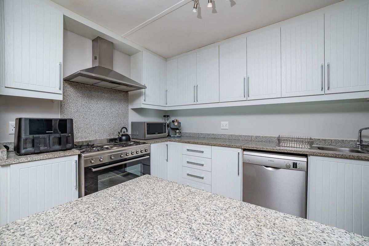 A functional kitchen featuring white cabinetry, granite countertops, a stainless steel gas stove with extractor fan, and an integrated dishwasher.