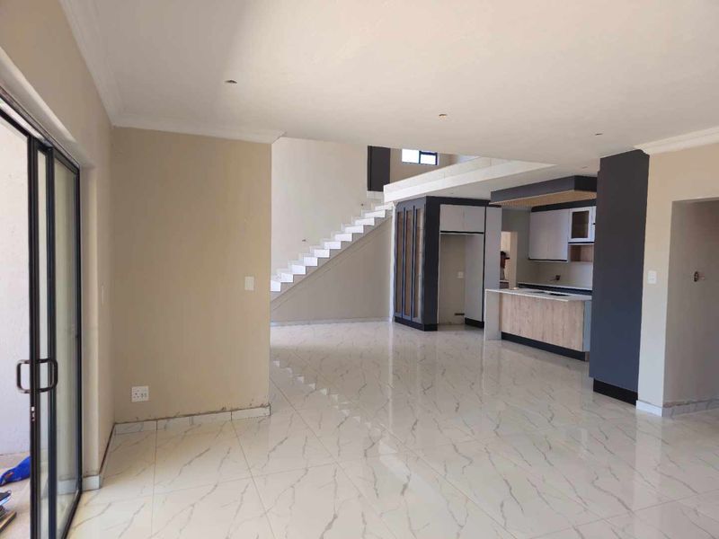Spacious open-plan living and kitchen area featuring modern marble-look tile flooring, a central kitchen island, and a staircase leading to the upper level.