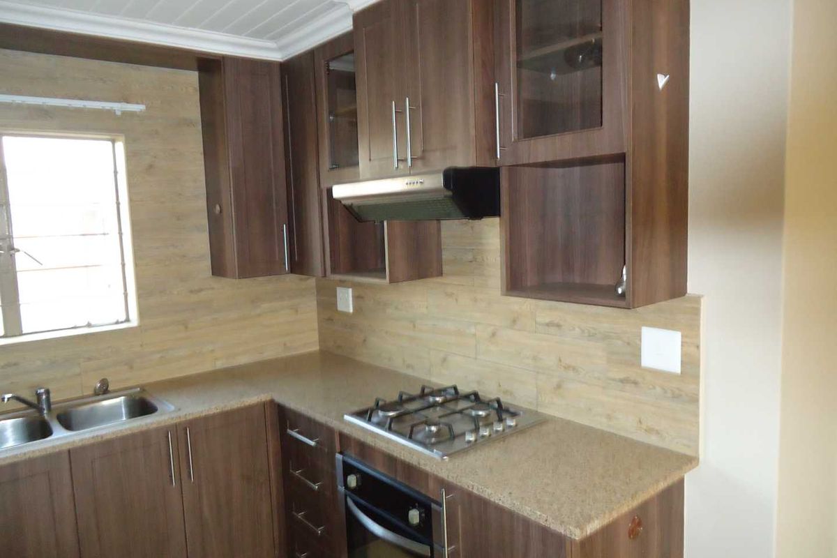 A functional kitchen featuring dark wood-look cabinetry, stone-effect countertops, a gas hob, built-in oven, and a wood-look tiled backsplash.