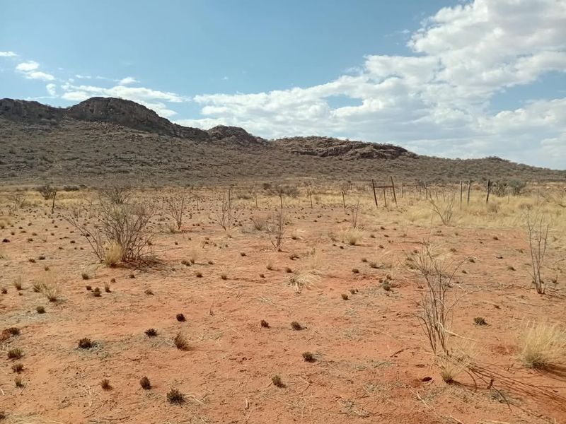 A wide-angle view of open agricultural land featuring arid terrain, sparse vegetation, and distant mountain ranges with existing wire fencing.