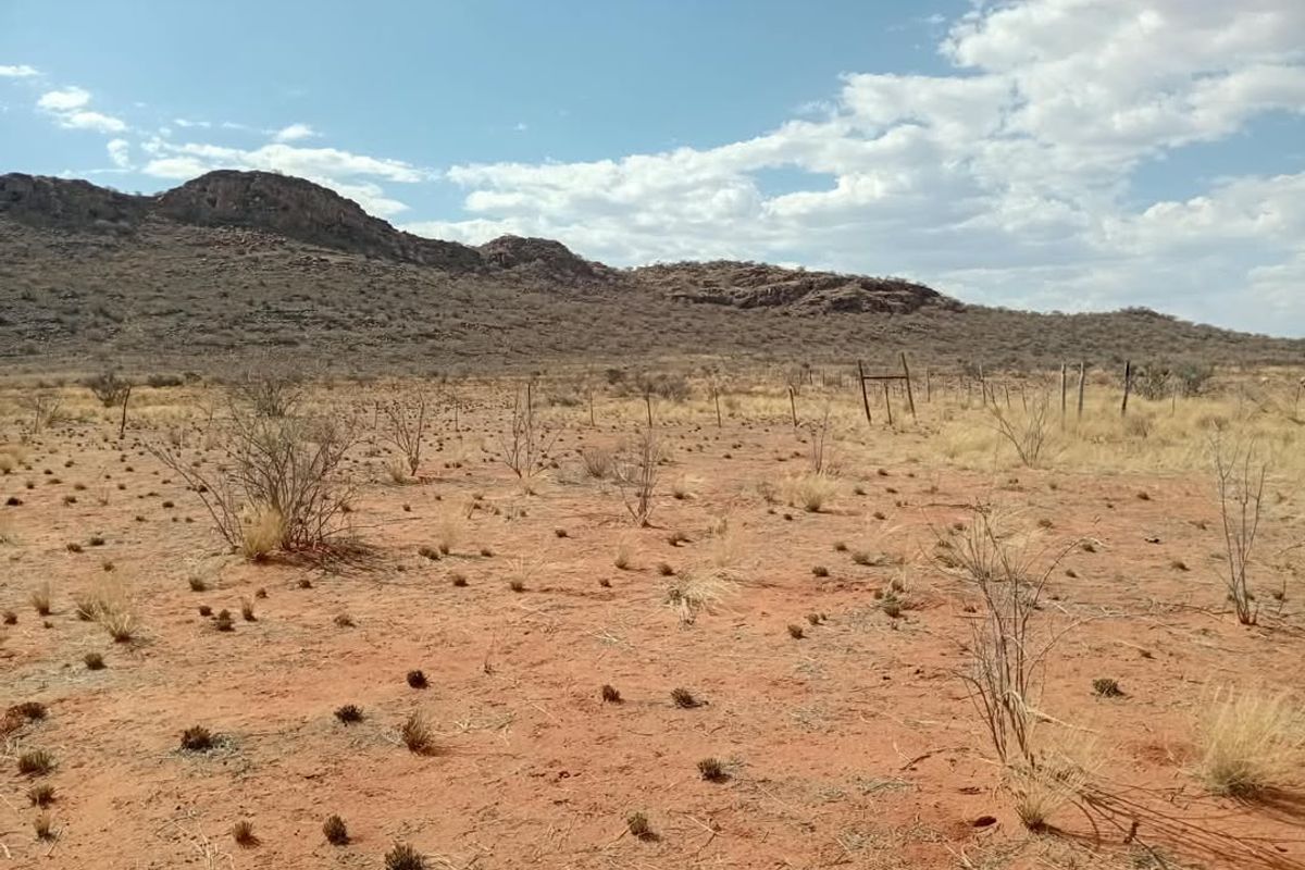 A wide-angle view of open agricultural land featuring arid terrain, sparse vegetation, and distant mountain ranges with existing wire fencing.