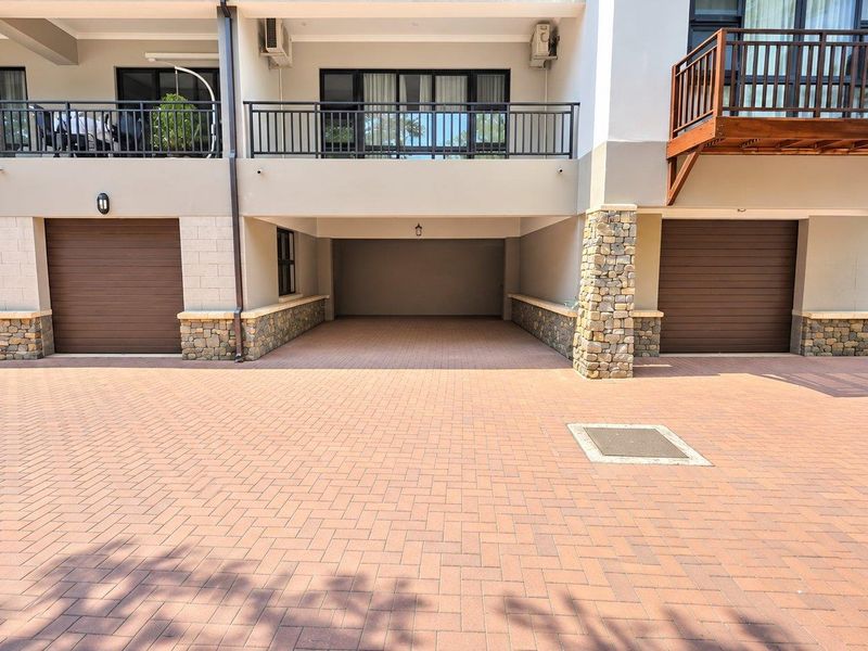 Exterior view of a multi-unit apartment complex featuring paved driveway access to multiple enclosed garages and upper-level balconies with metal railings.
