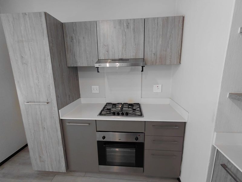 Modern kitchen featuring light wood-grain cabinetry, stone countertops, a built-in gas hob, oven, and stainless steel extractor fan.