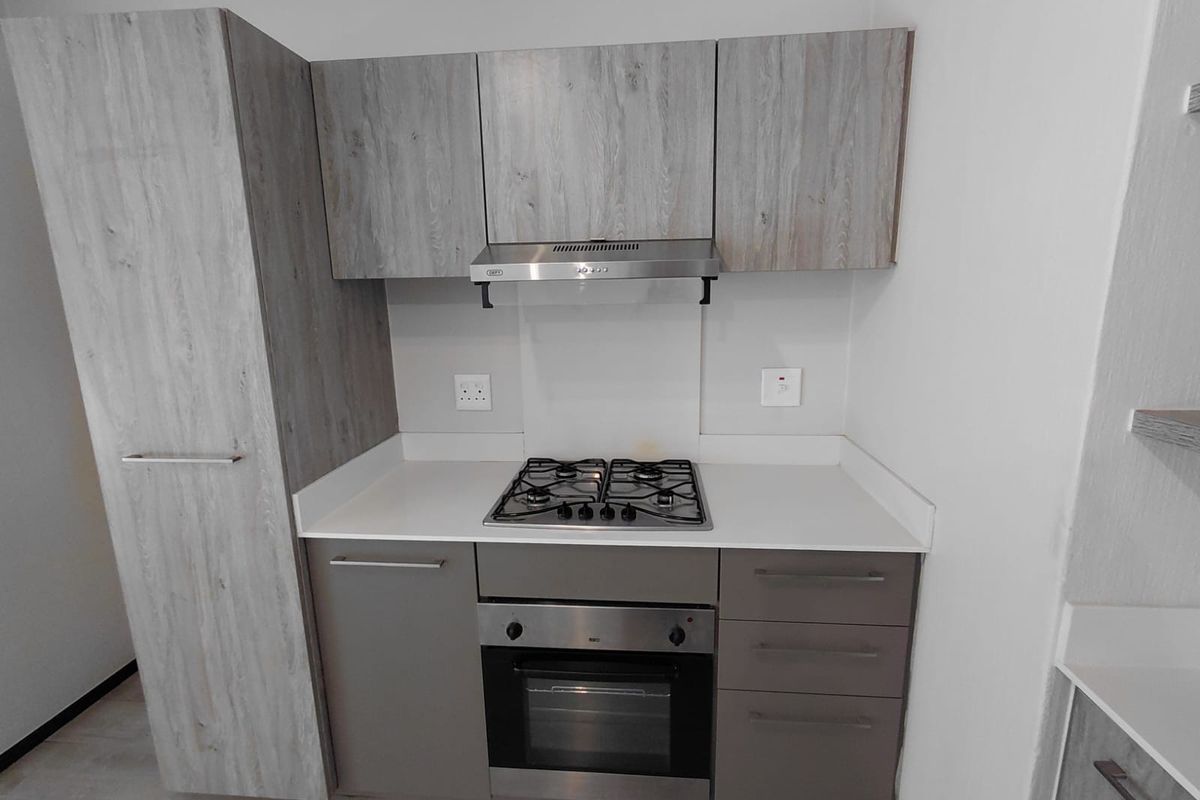 Modern kitchen featuring light wood-grain cabinetry, stone countertops, a built-in gas hob, oven, and stainless steel extractor fan.