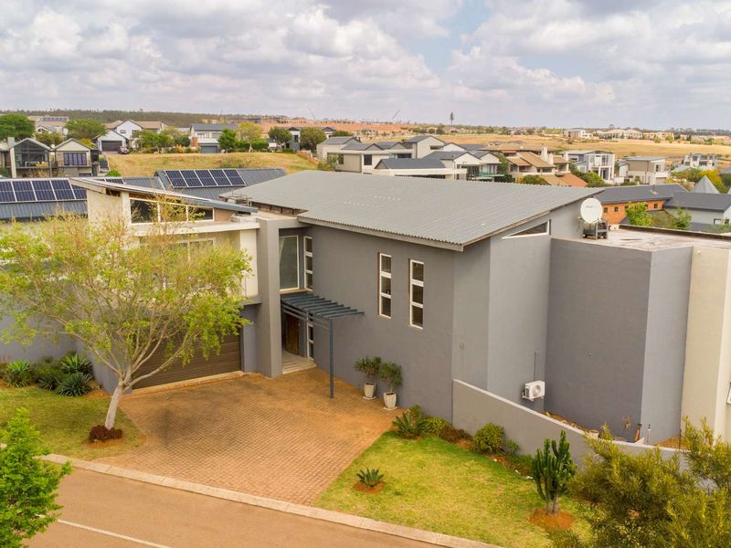Aerial view of a modern two-story residential property featuring a paved driveway, garage, solar panels, and a contemporary grey facade.