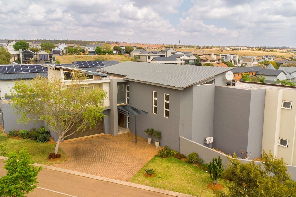 Aerial view of a modern two-story residential property featuring a paved driveway, garage, solar panels, and a contemporary grey facade.