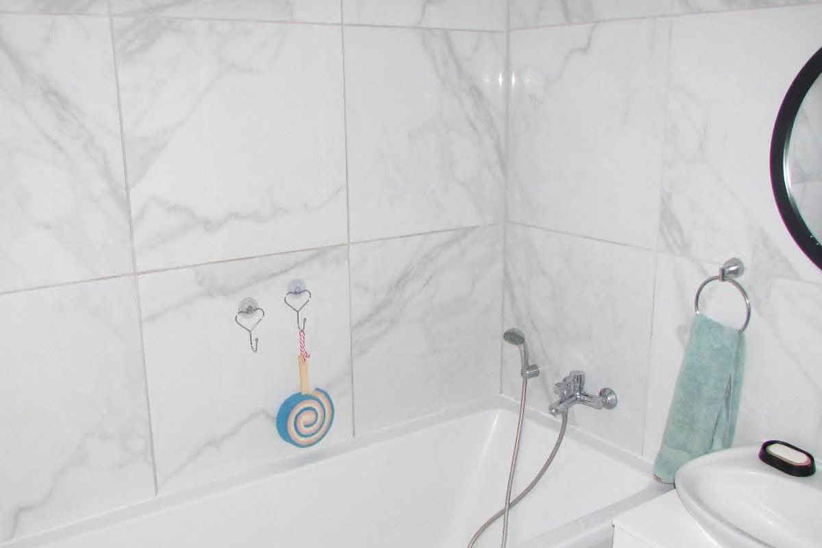 A modern bathroom featuring white marble-effect wall tiles, a built-in bathtub with a handheld shower mixer, and a vanity basin.