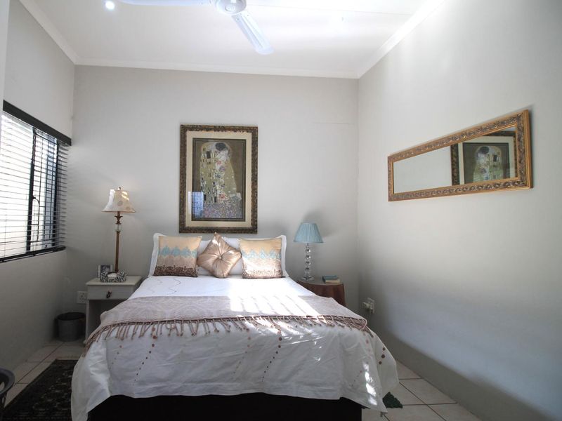 A well-maintained bedroom featuring neutral walls, tiled flooring, a ceiling fan, and venetian blinds for privacy.