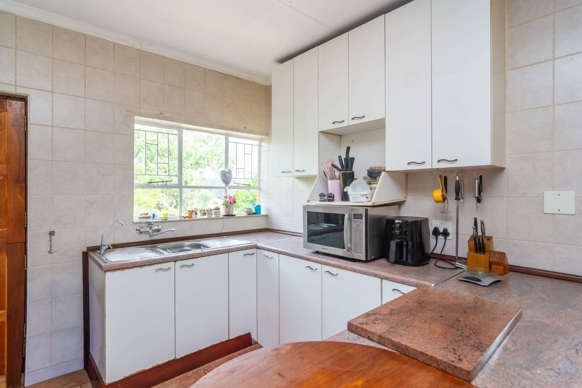 A functional kitchen featuring white cabinetry, laminate countertops, a double-basin sink, and tiled walls with a window overlooking the garden.