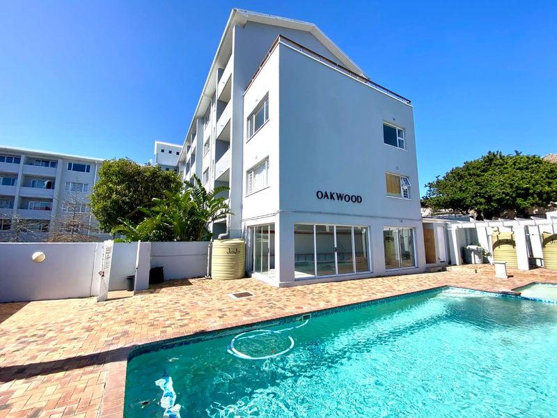 Exterior view of the Oakwood apartment complex featuring a swimming pool, paved patio area, and water storage tanks.