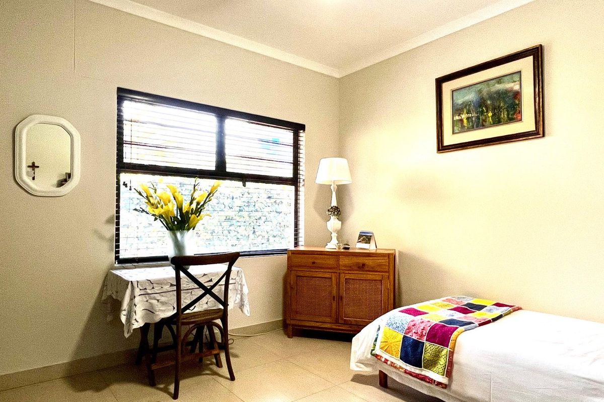 A well-lit bedroom featuring neutral tiled flooring, coved cornicing, and venetian blinds, offering a comfortable and functional living space.