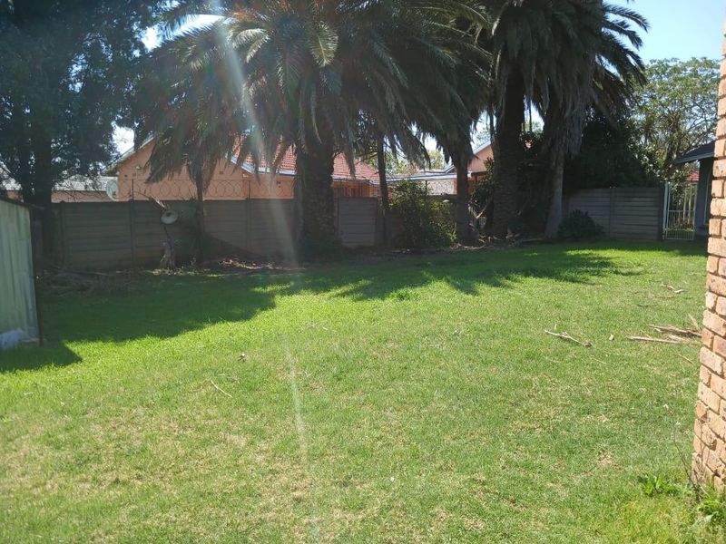 A spacious rear garden featuring a well-maintained lawn, mature palm trees, and secure perimeter fencing with razor wire.