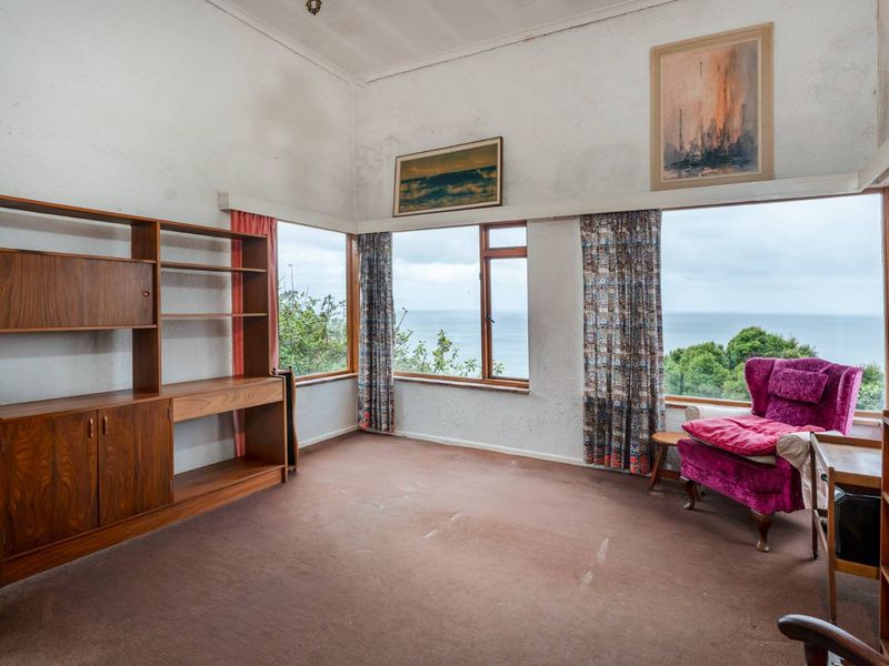 Spacious living room featuring large corner windows with expansive ocean views, high ceilings, and carpeted flooring, offering significant potential for modernization.