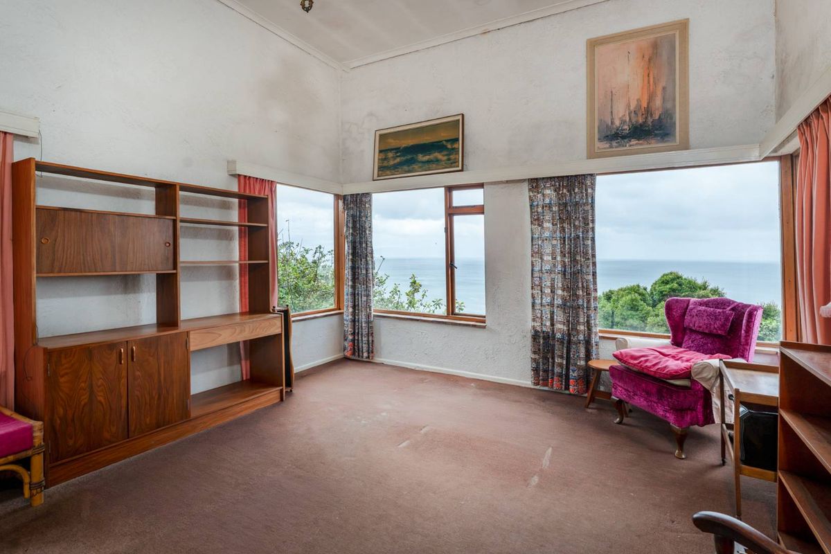 Spacious living room featuring large corner windows with expansive ocean views, high ceilings, and carpeted flooring, offering significant potential for modernization.