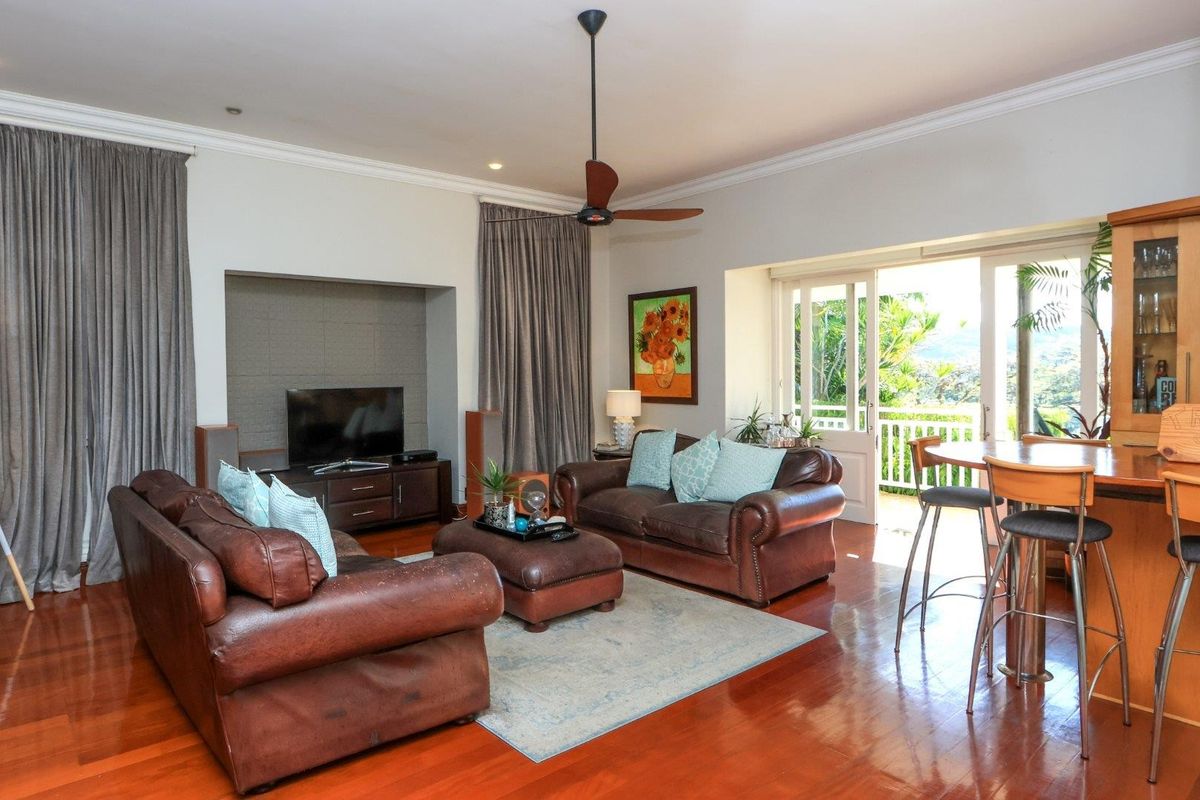 Spacious living room featuring polished hardwood floors, a built-in bar, ceiling fan, and direct access to an outdoor patio through glass french doors.