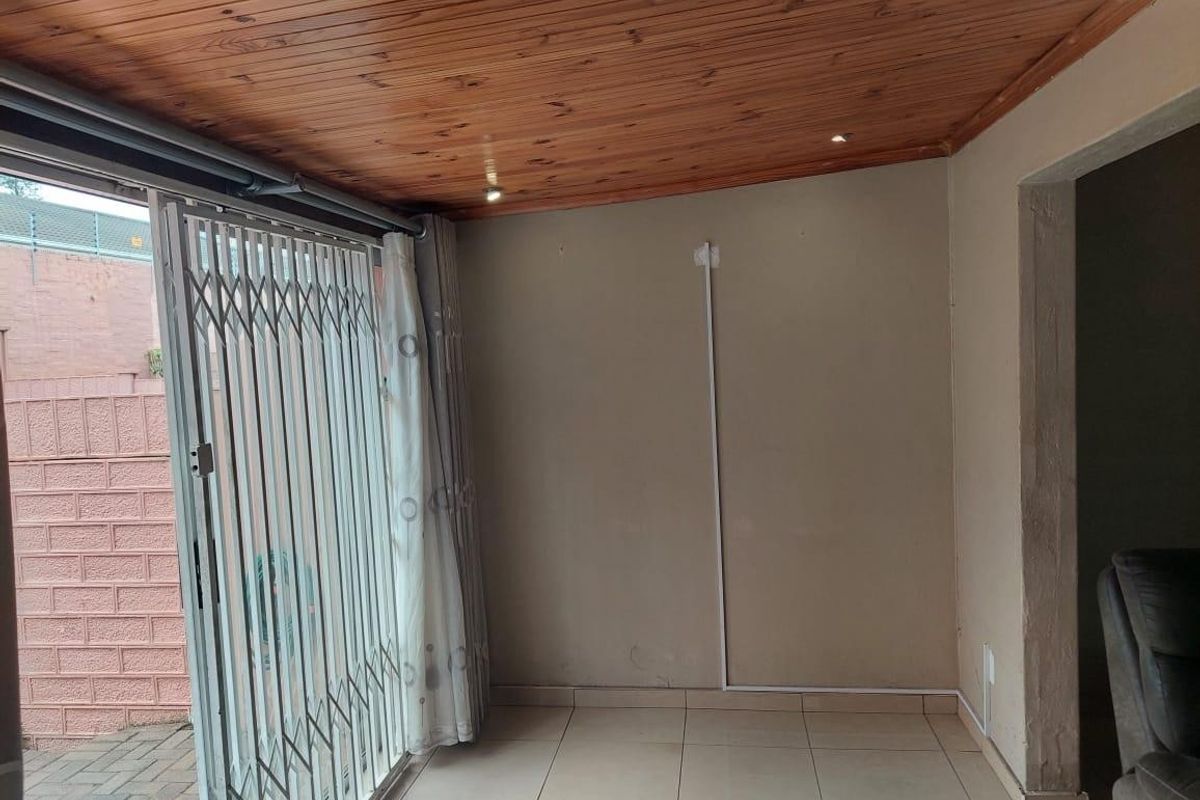 An open-plan living area featuring ceramic floor tiles, a timber tongue and groove ceiling, and a retractable security gate leading to the exterior.