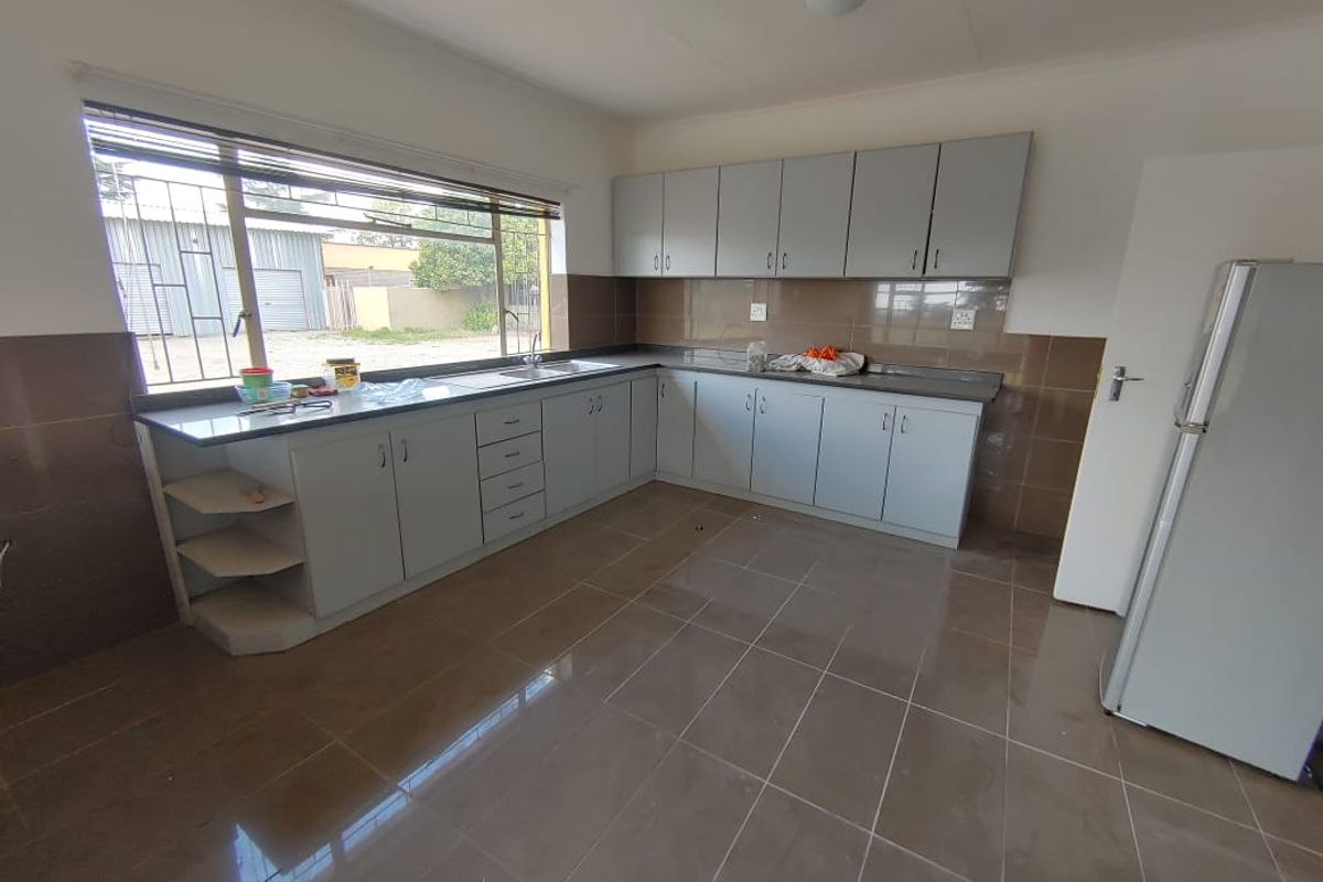 A functional, empty kitchen featuring ample built-in cabinetry, tiled flooring, a stainless steel sink, and a large window with security bars.