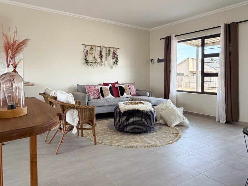 Bright open-plan living area featuring neutral tiled flooring, clean wall finishes, and a large window providing natural light.