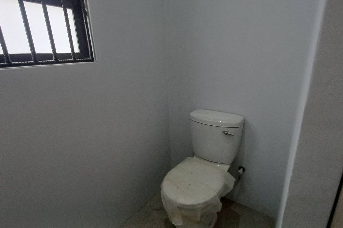 A compact bathroom featuring a standard toilet and a window with security bars, presenting a clean but basic and unfinished aesthetic.