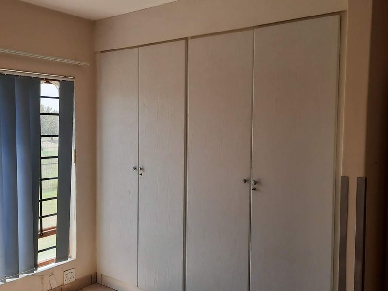 A bedroom featuring built-in cupboards and vertical blinds, providing a clean and functional space.