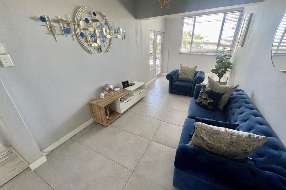 A bright living room featuring large windows, neutral floor tiles, and a clean, functional layout suitable for relaxation.