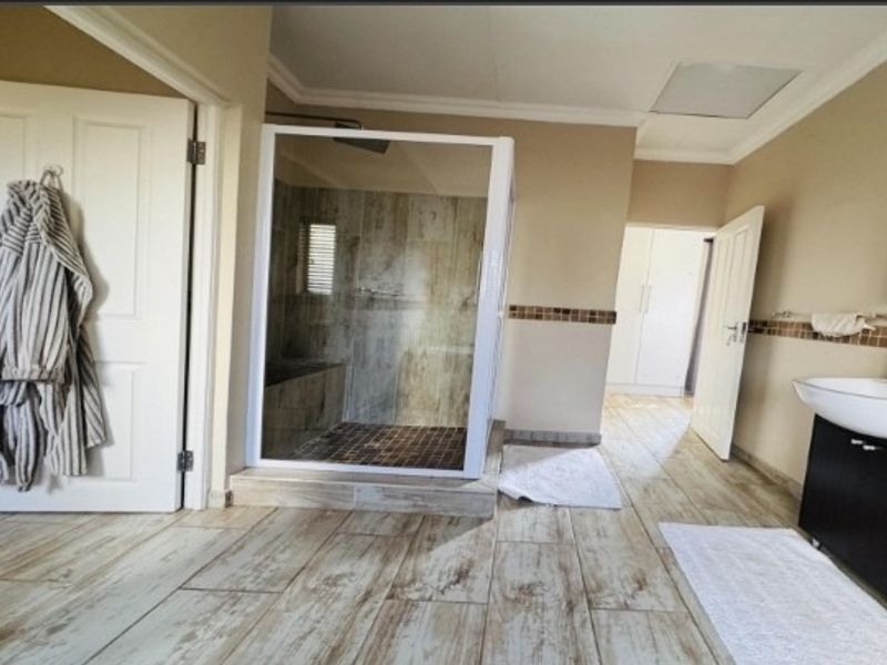 A spacious bathroom featuring a walk-in shower, modern vanity with basin, and tiled flooring, offering a functional and well-maintained layout.