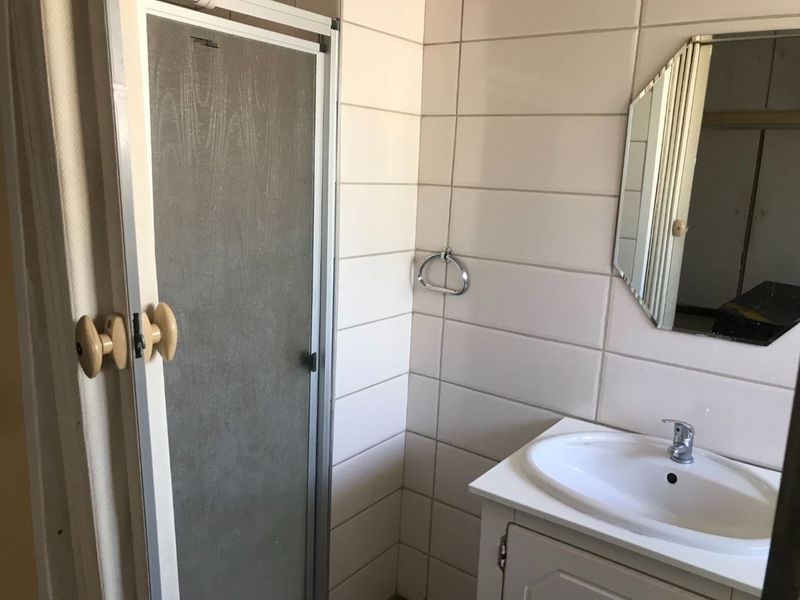 A compact bathroom featuring a shower enclosure, a vanity cabinet with a basin, and wall-mounted mirror, presenting an opportunity for modern renovation.