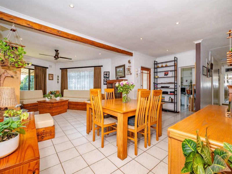 Spacious open-plan living and dining area featuring tiled flooring, an exposed timber ceiling beam, and recessed downlighting, creating a functional and connected living space.
