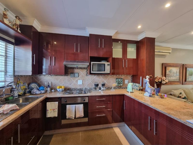 A well-maintained kitchen featuring dark wood cabinetry, granite countertops, integrated appliances, and a tiled backsplash with a breakfast bar area.