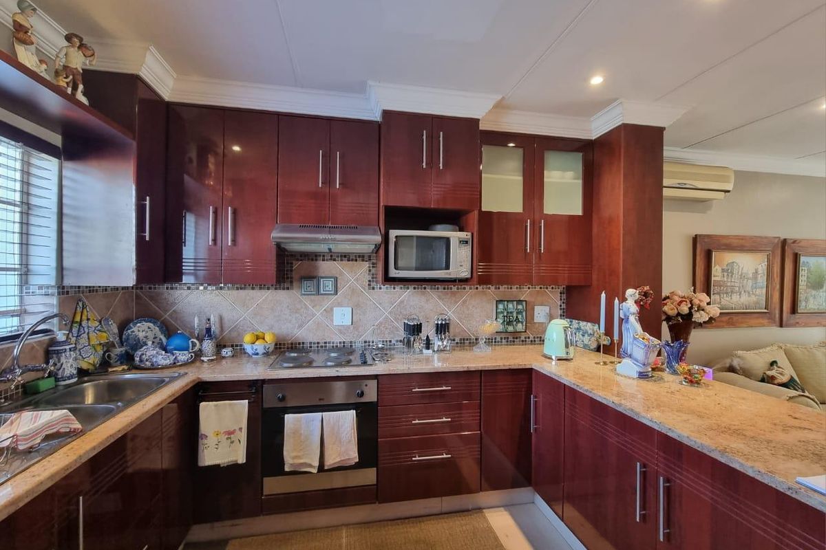 A well-maintained kitchen featuring dark wood cabinetry, granite countertops, integrated appliances, and a tiled backsplash with a breakfast bar area.