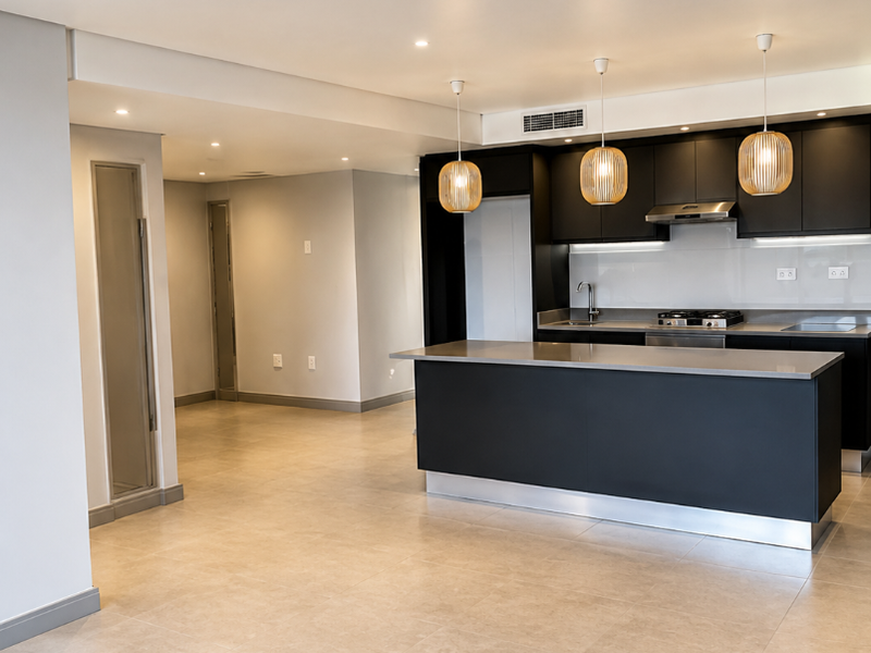 Modern open-plan kitchen featuring a sleek island, dark cabinetry, integrated appliances, and neutral tiled flooring in a spacious, well-lit living area.