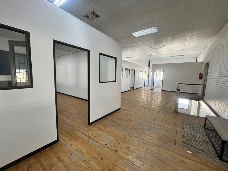 Spacious open-plan office area featuring timber flooring, suspended ceilings with recessed lighting, and multiple partitioned office rooms.