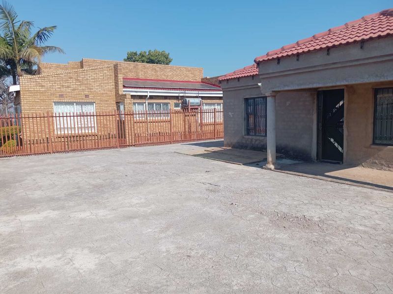 Exterior view of the property featuring a large concrete driveway, security fencing, and a covered porch area with a tiled roof.