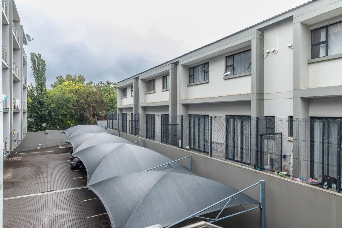 Rear view of the townhouse complex featuring a paved parking area with shade cloth carports and secure perimeter fencing.