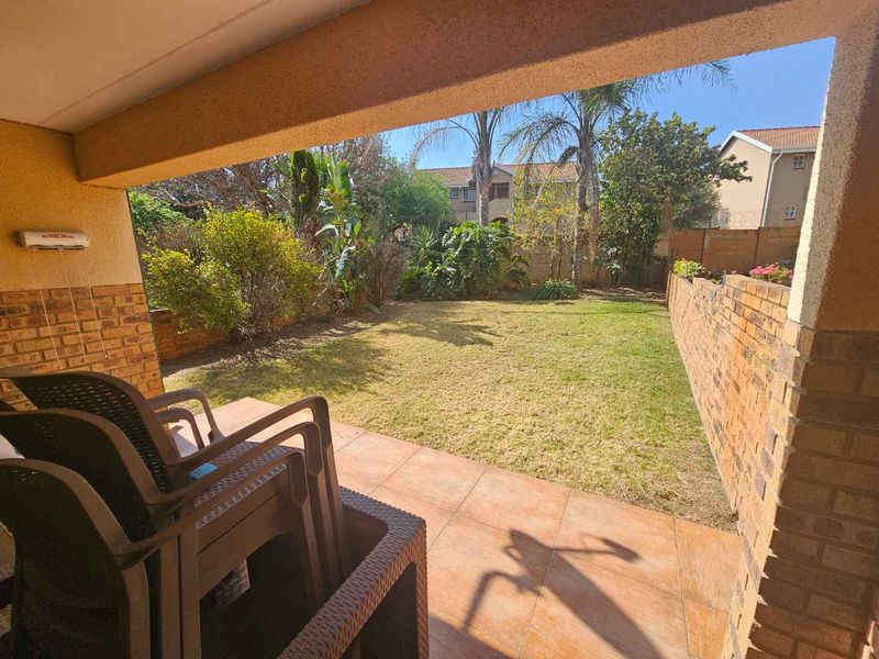 A covered patio area with tiled flooring and a brick boundary wall, overlooking a private garden space.